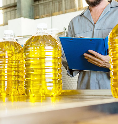 Photo of a man holding a clipboard doing QA on bottles of oil